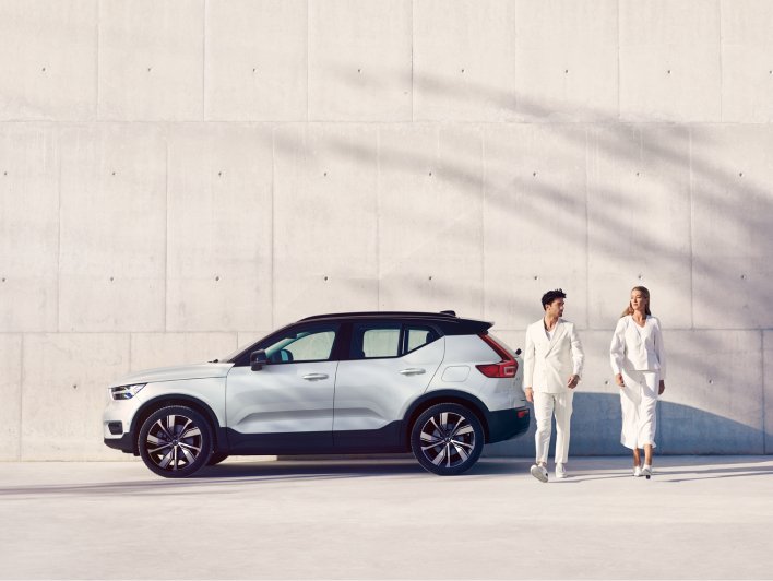 Image of XC40 recharge in a concept location. There is a man and woman in the picture with a shadow of a tree in the background. The tonality of this image is set in light beige and white.