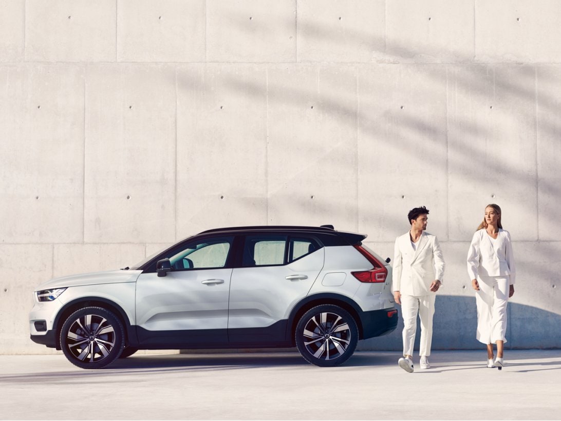 Image of XC40 recharge in a concept location. There is a man and woman in the picture with a shadow of a tree in the background. The tonality of this image is set in light beige and white.