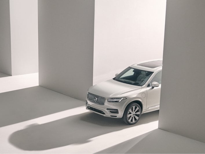 Image of XC90 in beige studio environment. The image is only showing the front half of the car. There is lots of light play, and dramatic long shadows.