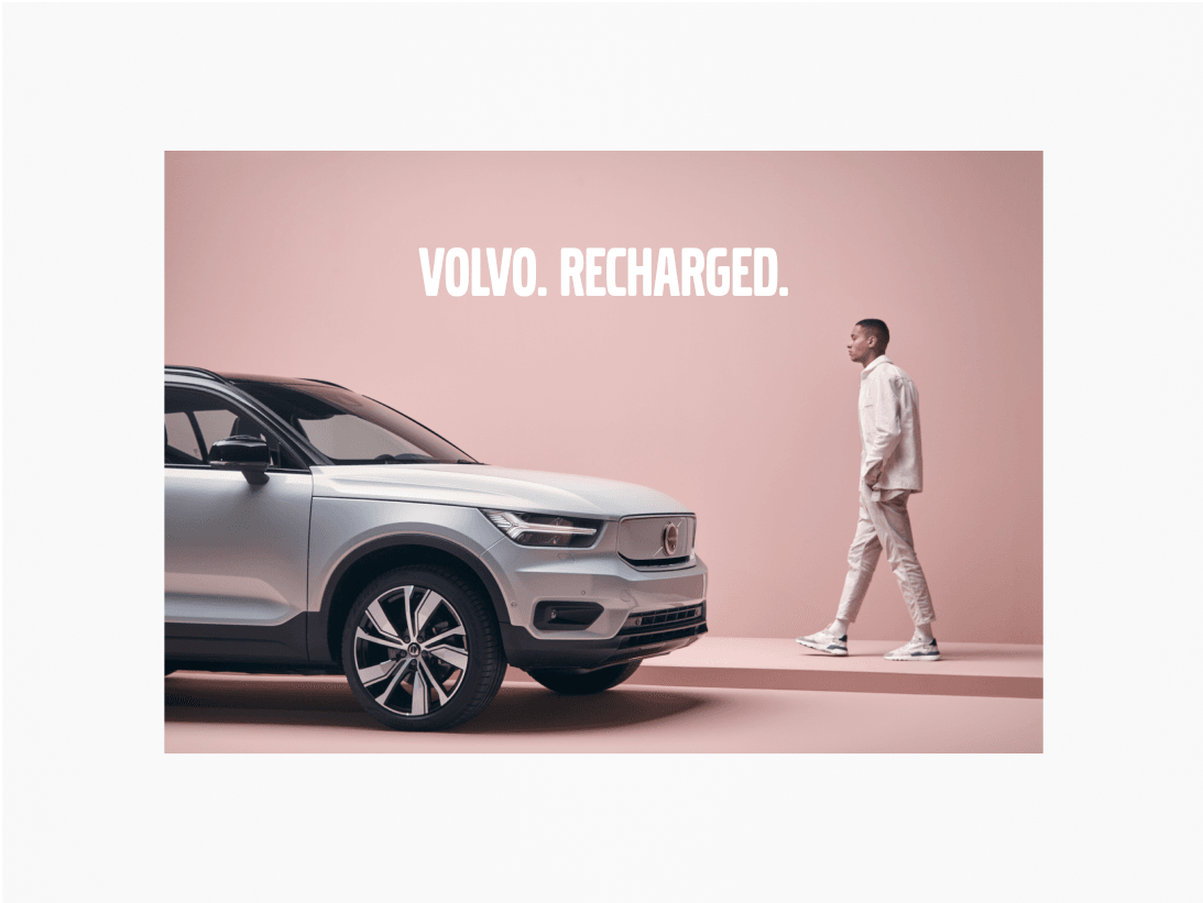 Example of Volvo Broad heading included over an image of an XC40, shot in a pink studio setting. There is a male walking in the background, approaching the vehicle. The heading is set in white.